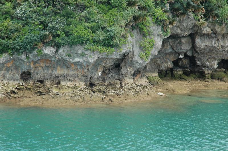 久米島の海岸の岩壁にあいた洞窟と、エメラルド色の浅い海